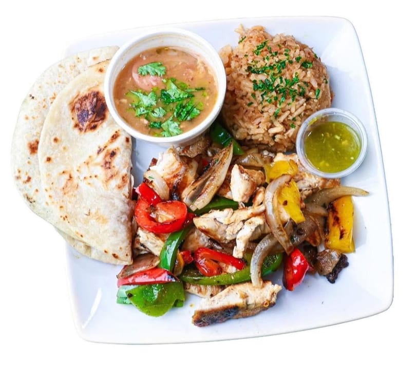 Chicken fajitas with bell peppers and onions, rice, beans, salsa, and tortillas on a white plate.