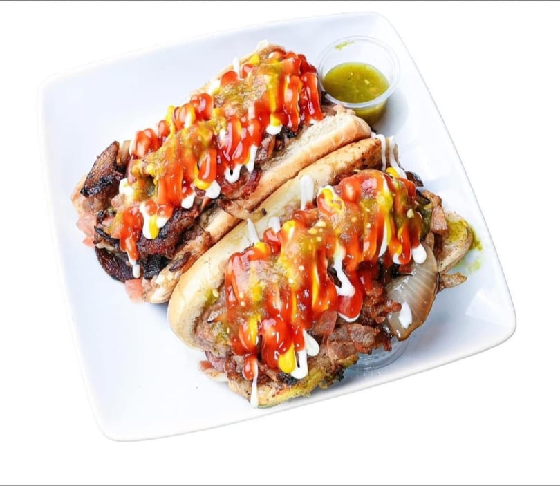 Two loaded hot dogs with various toppings and sauces, served on a white rectangular plate.